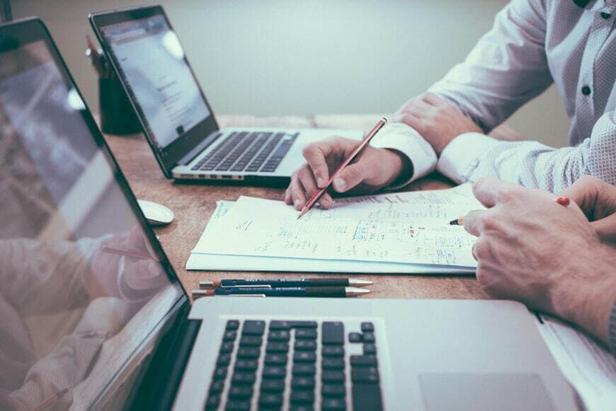Two people working together at a desk with laptops and documents during a business meeting.