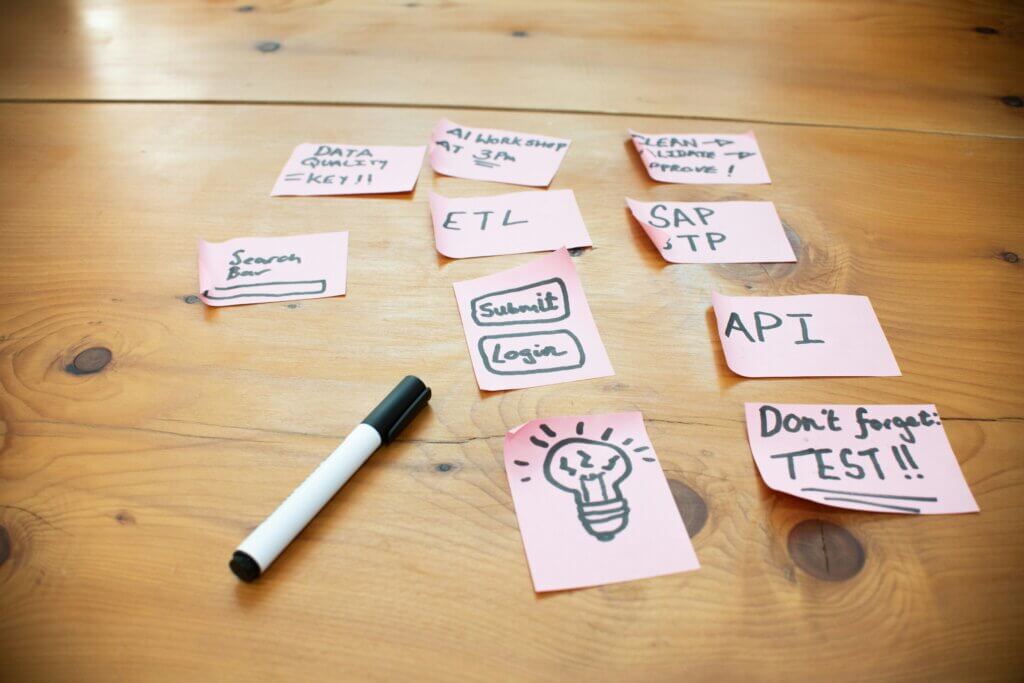 Pink sticky notes on a wooden table detailing technical requirements like data quality, ETL, and APIs for planning AI Proofs of Concept.